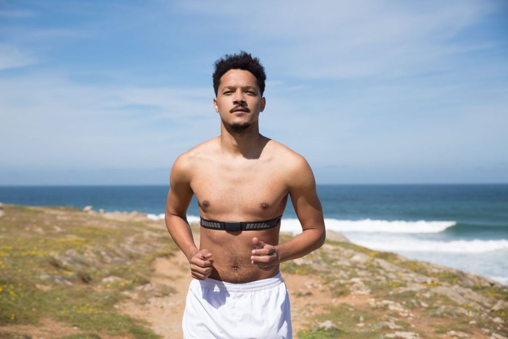 Coureur torse nu portant une ceinture cardiaque au bord de la mer