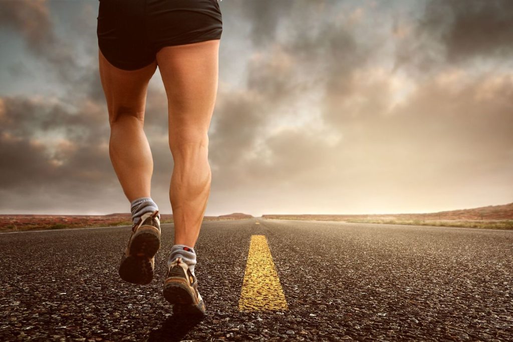 Jambes d’un coureur en pleine foulée sur une route goudronnée