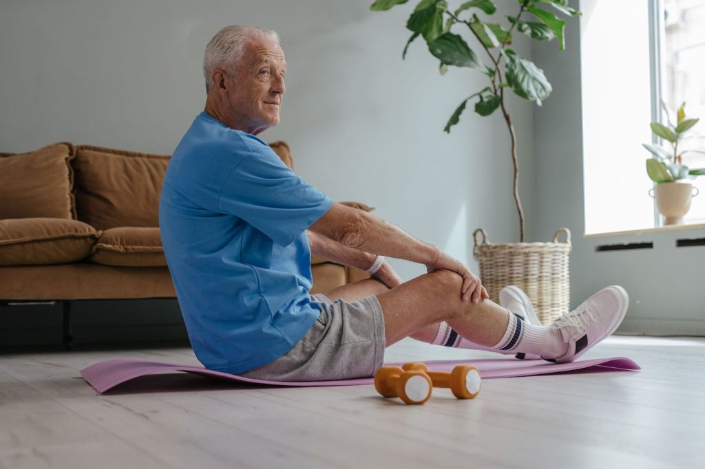 Homme âgé qui s’étire sur un tapis dans son salon