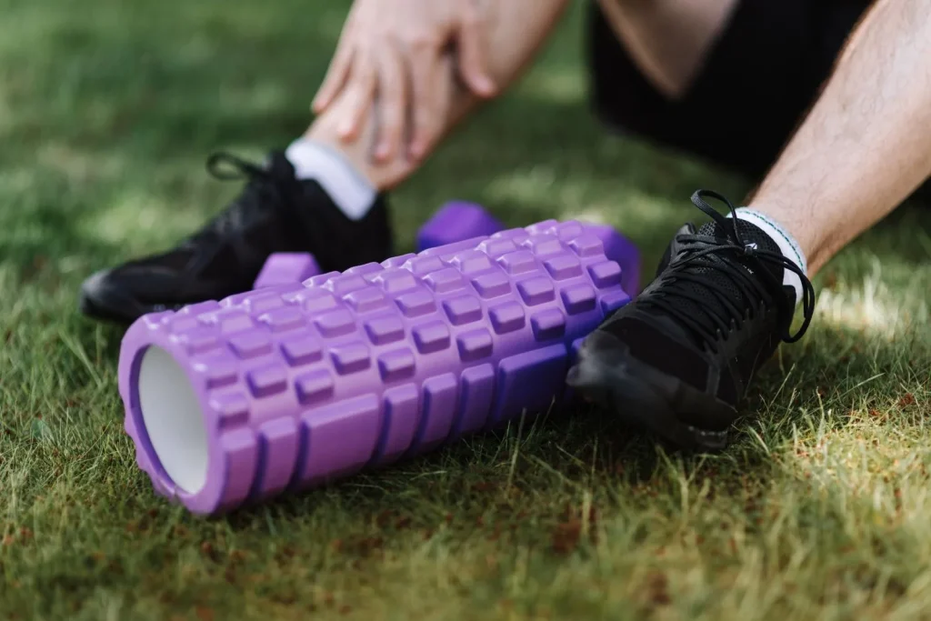 Rouleau de massage posé dans l'herbe entre les chaussures d'un coureur assis