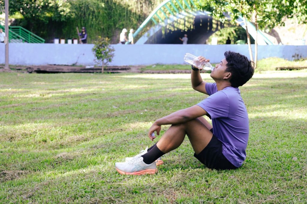 Coureur assis dans l’herbe qui boit à sa gourde après l’effort