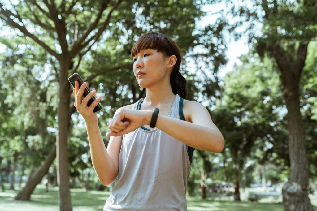 Coureuse qui consulte son téléphone et sa montre dans un parc