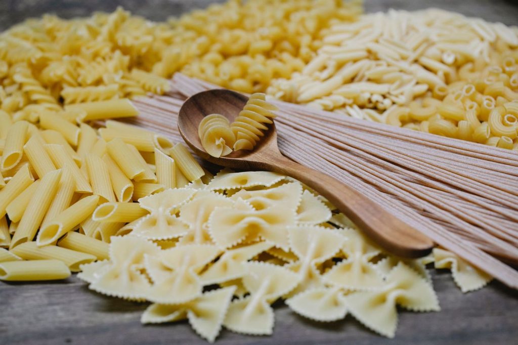 Pâtes crues de plusieurs formes sur une table, cuillère en bois