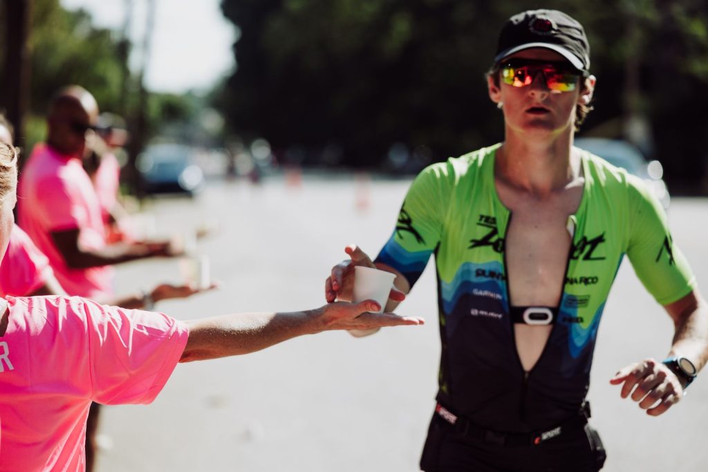 Coureur qui saisit un gobelet tendu par une bénévole à un ravitaillement, en pleine course
